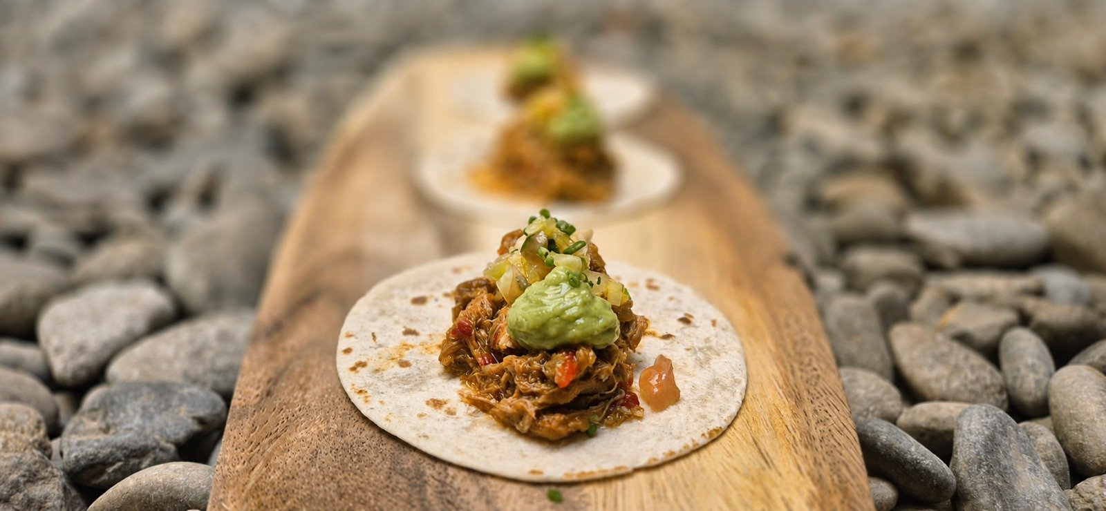 Taco de Ternasco de Aragón al pastor con guacamole y pico de gallo sobre una tabla de madera.