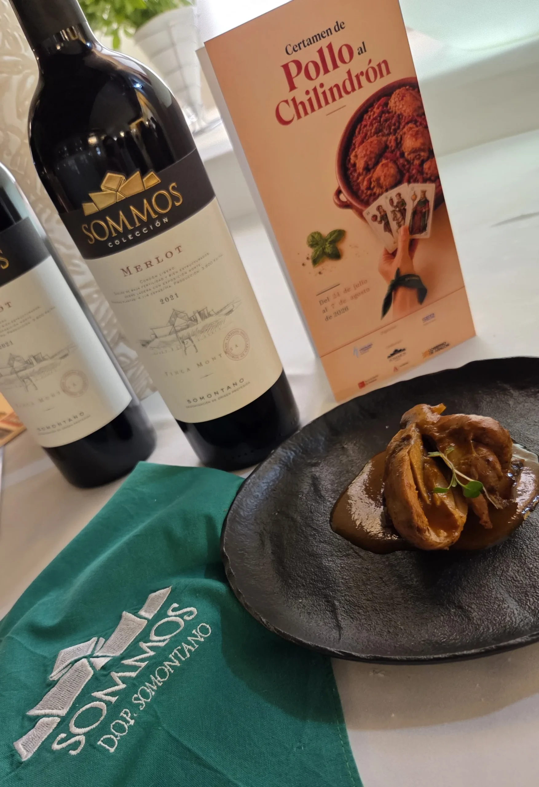 Plato de pollo al chilindrón de Las Torres junto a botellas de vino Sommos y el cartel del certamen



